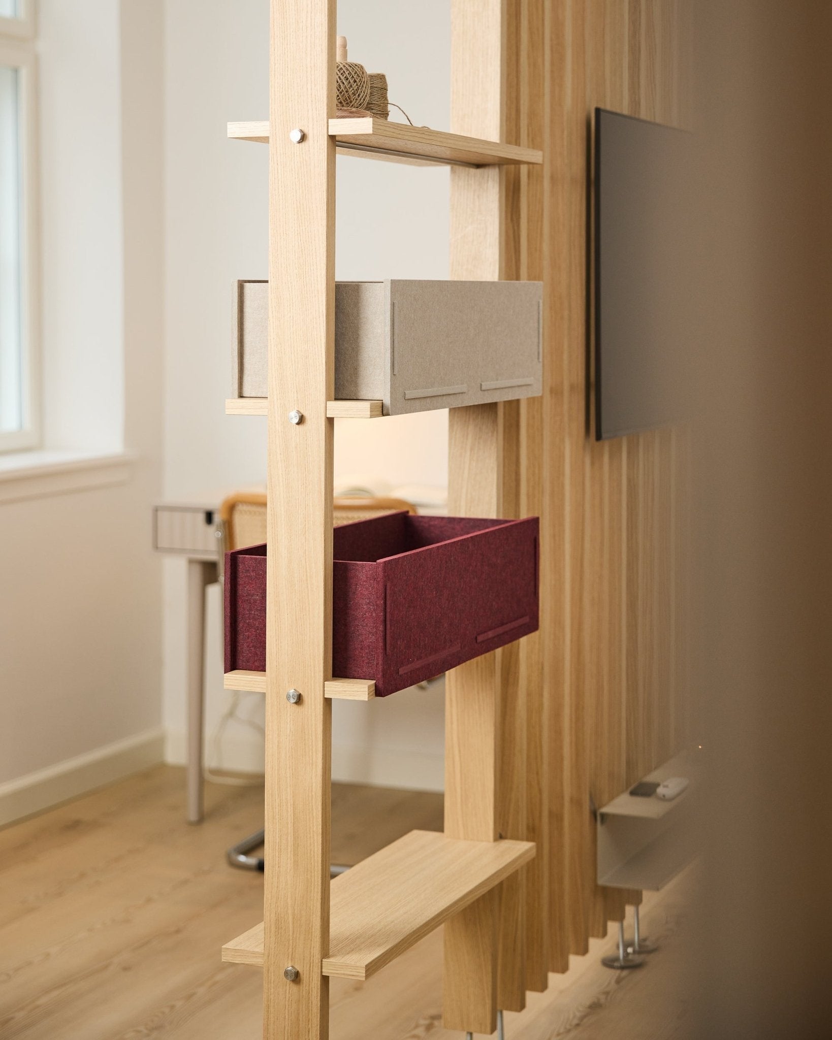 En hylle fra WoodUpp viser en oppbevaringsboks i beige og en ox red Vigg Felt Box / BM2 i et lyst, minimalistisk nordisk rom med akustiske tredetaljer.